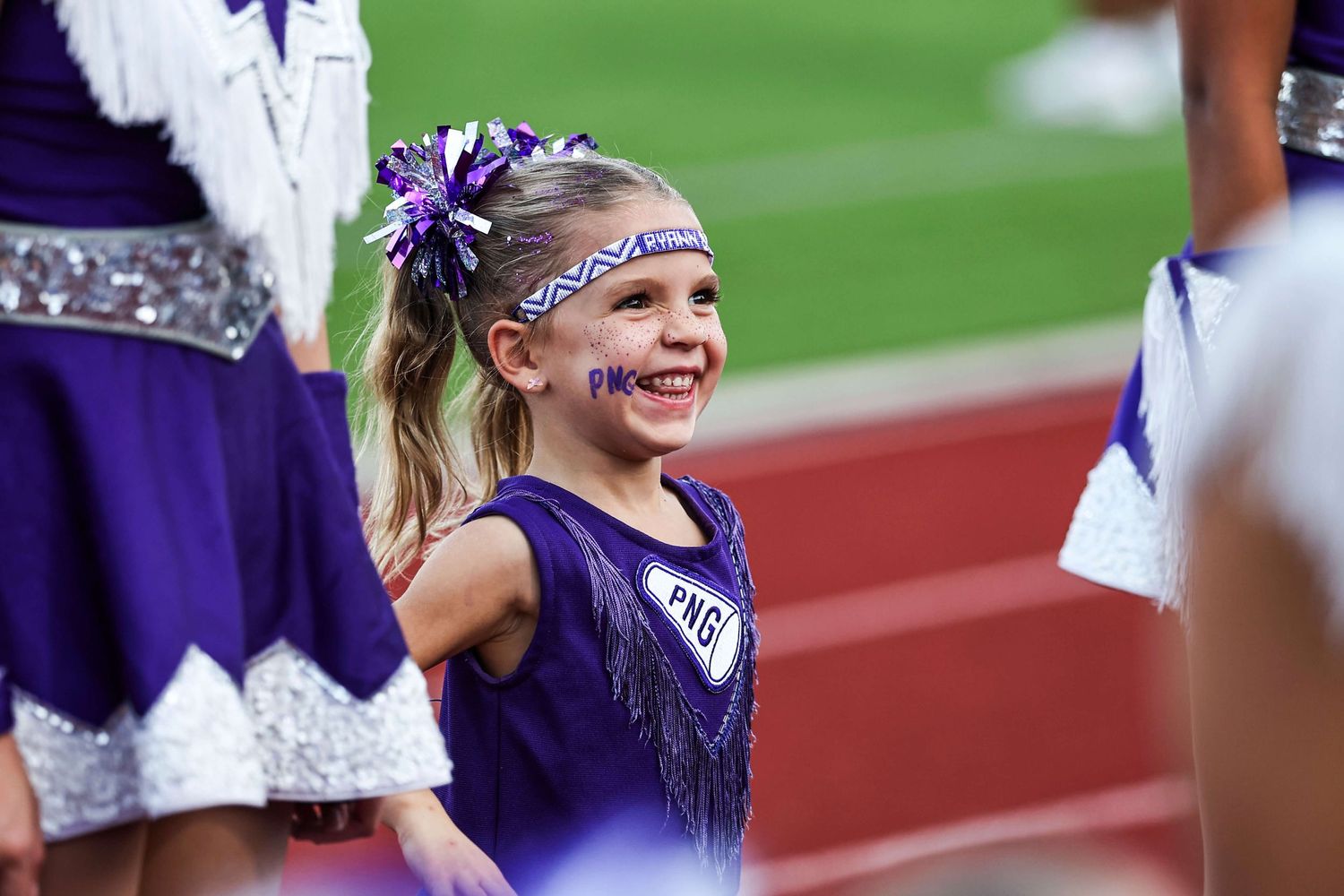 Cheerleader in purple uniform smiling during game on athletic field.