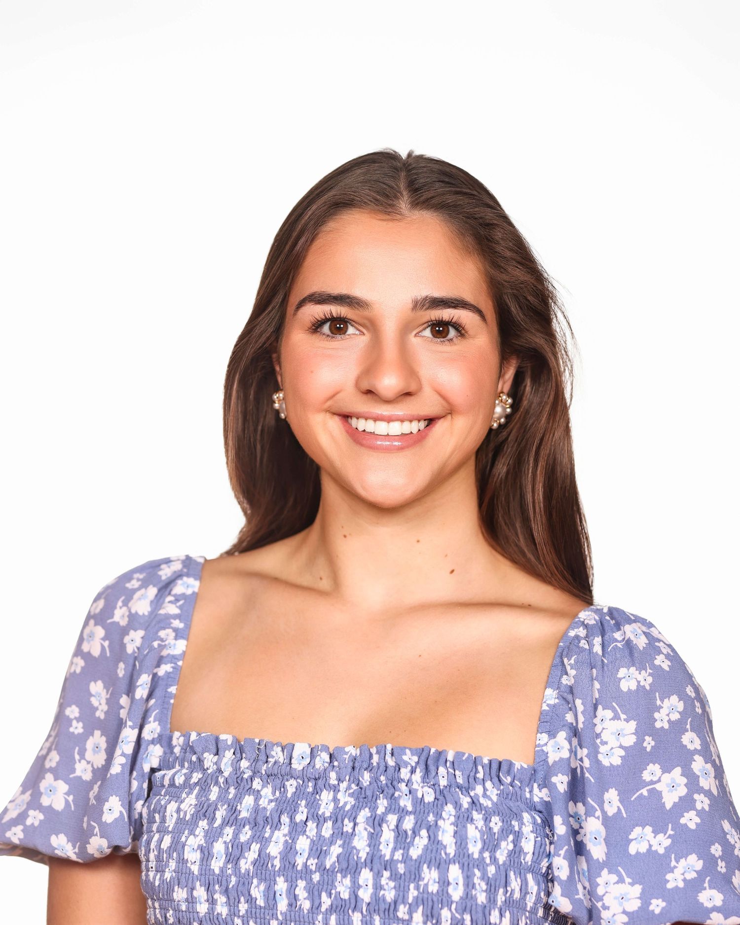 Woman wearing a purple floral print dress with puff sleeves smiles at camera in a bright studio setting.
