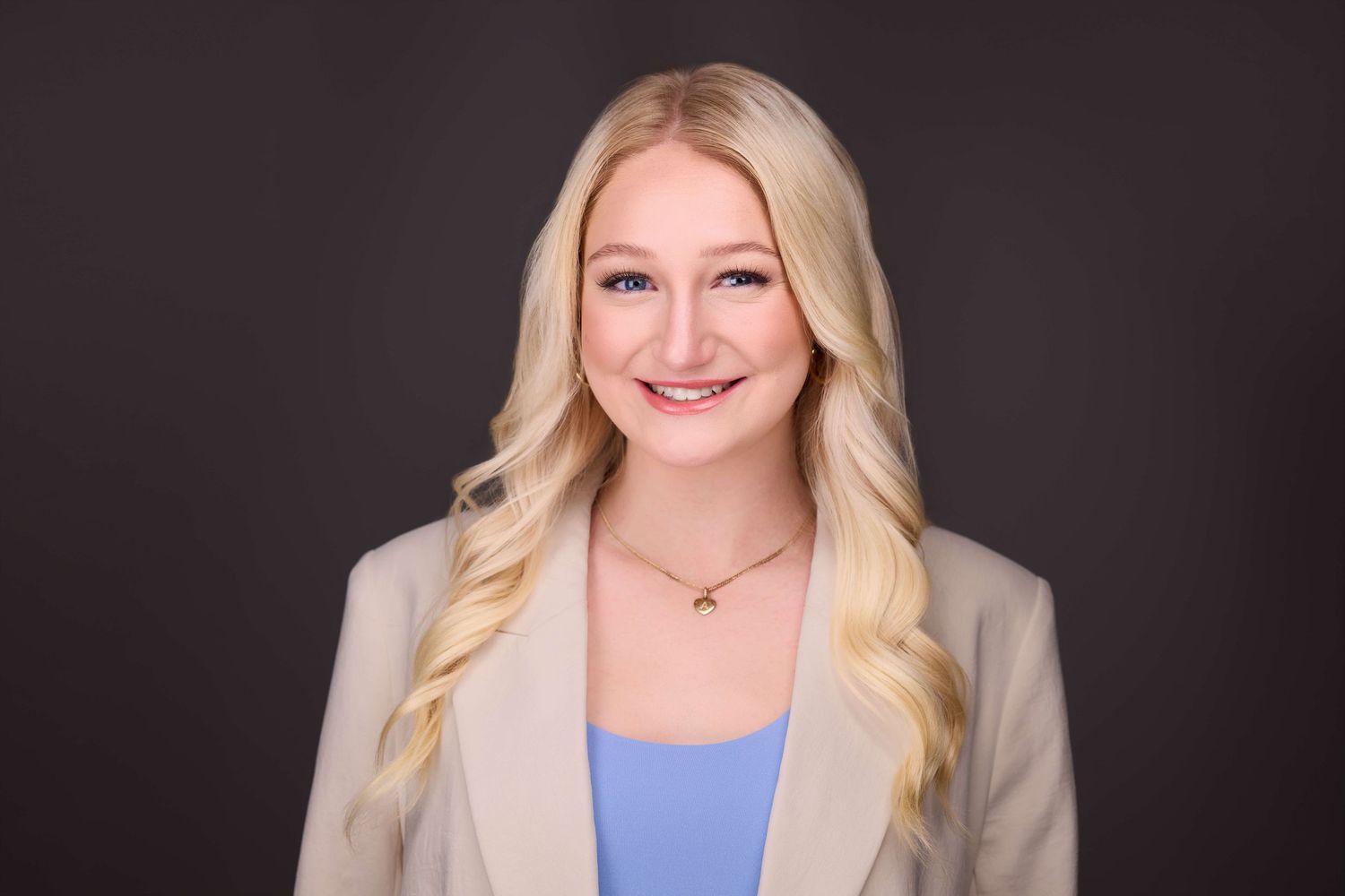 Professional portrait of someone in business attire with light blue top against dark background.