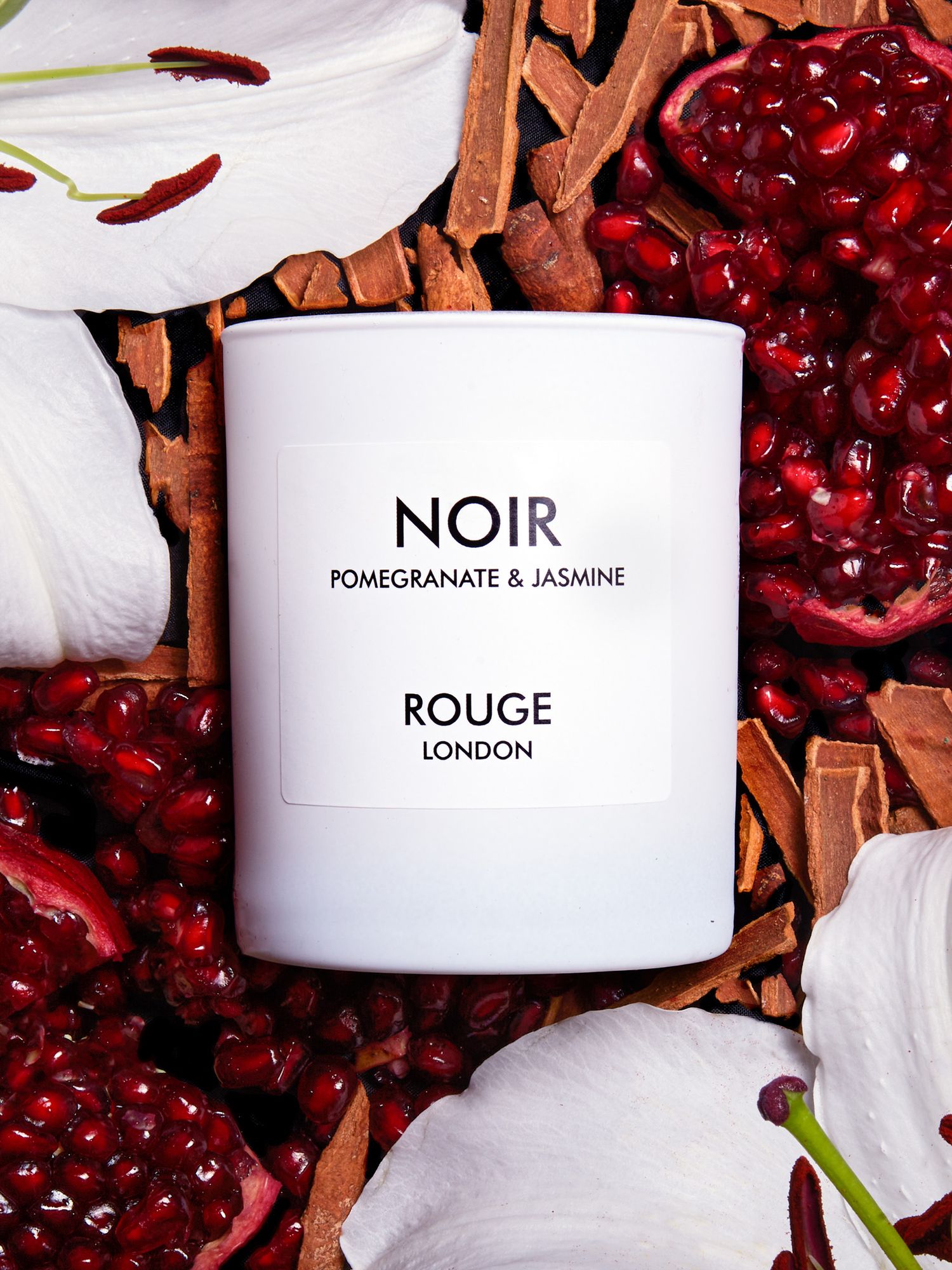 White Rouge London candle with pomegranate and jasmine fragrance displayed among cinnamon sticks and berries.
