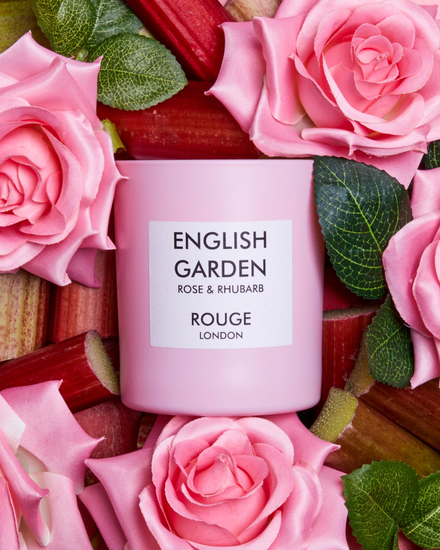 Rouge London English Garden candles displayed with fresh pink roses and rhubarb stems.