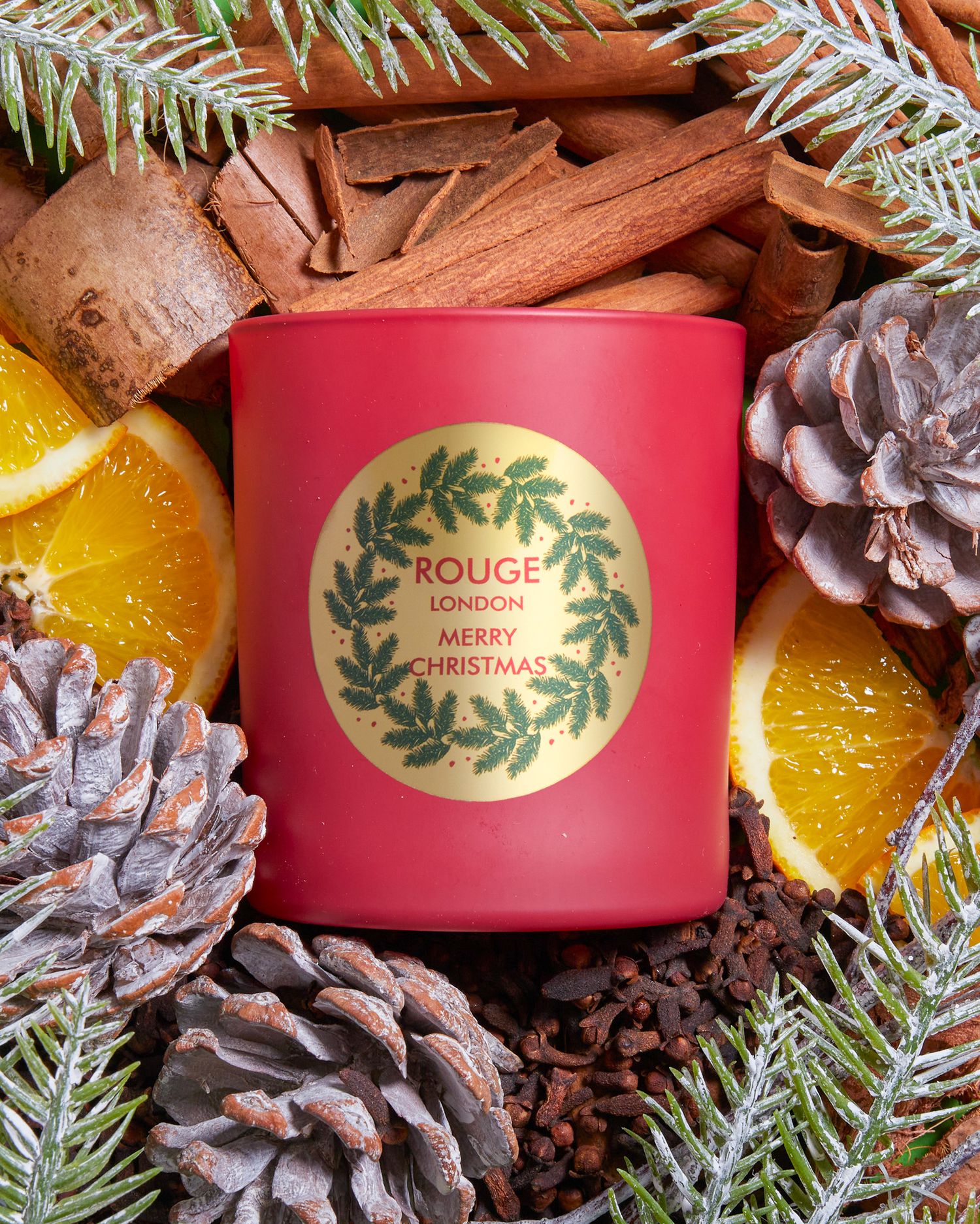 Festive holiday candle display with pinecones, oranges, and evergreen branches.