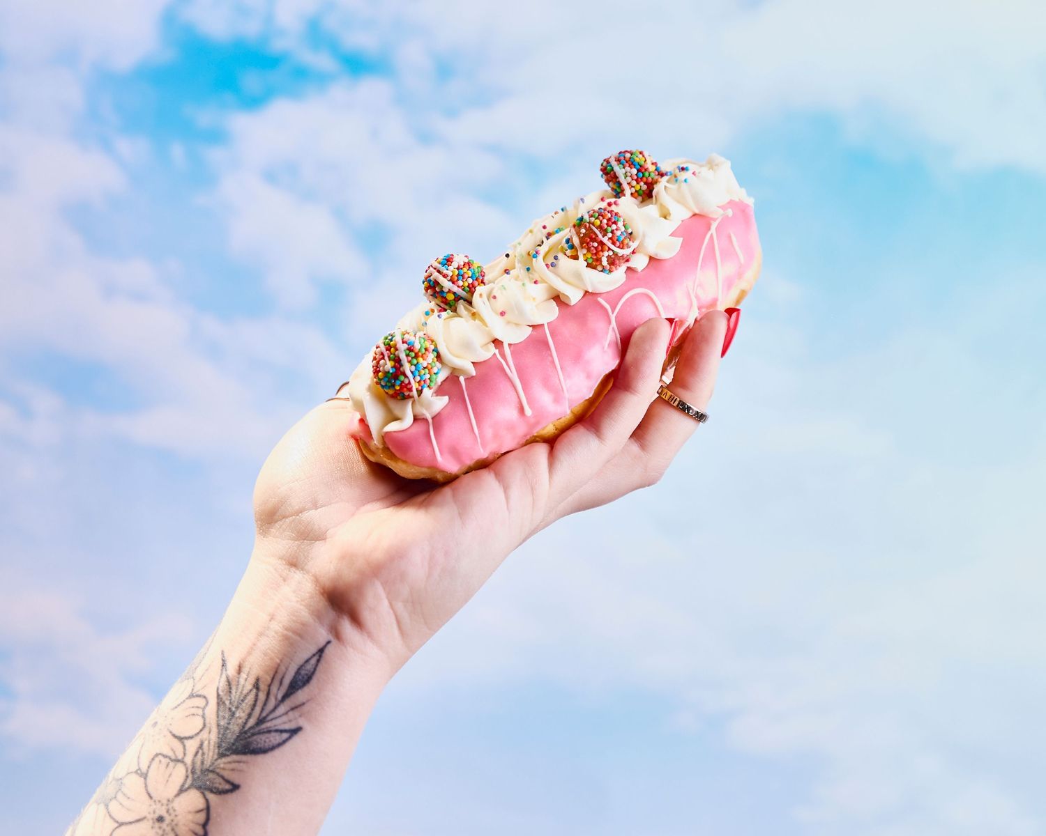 Pink frosted dessert being held against a blue sky background.