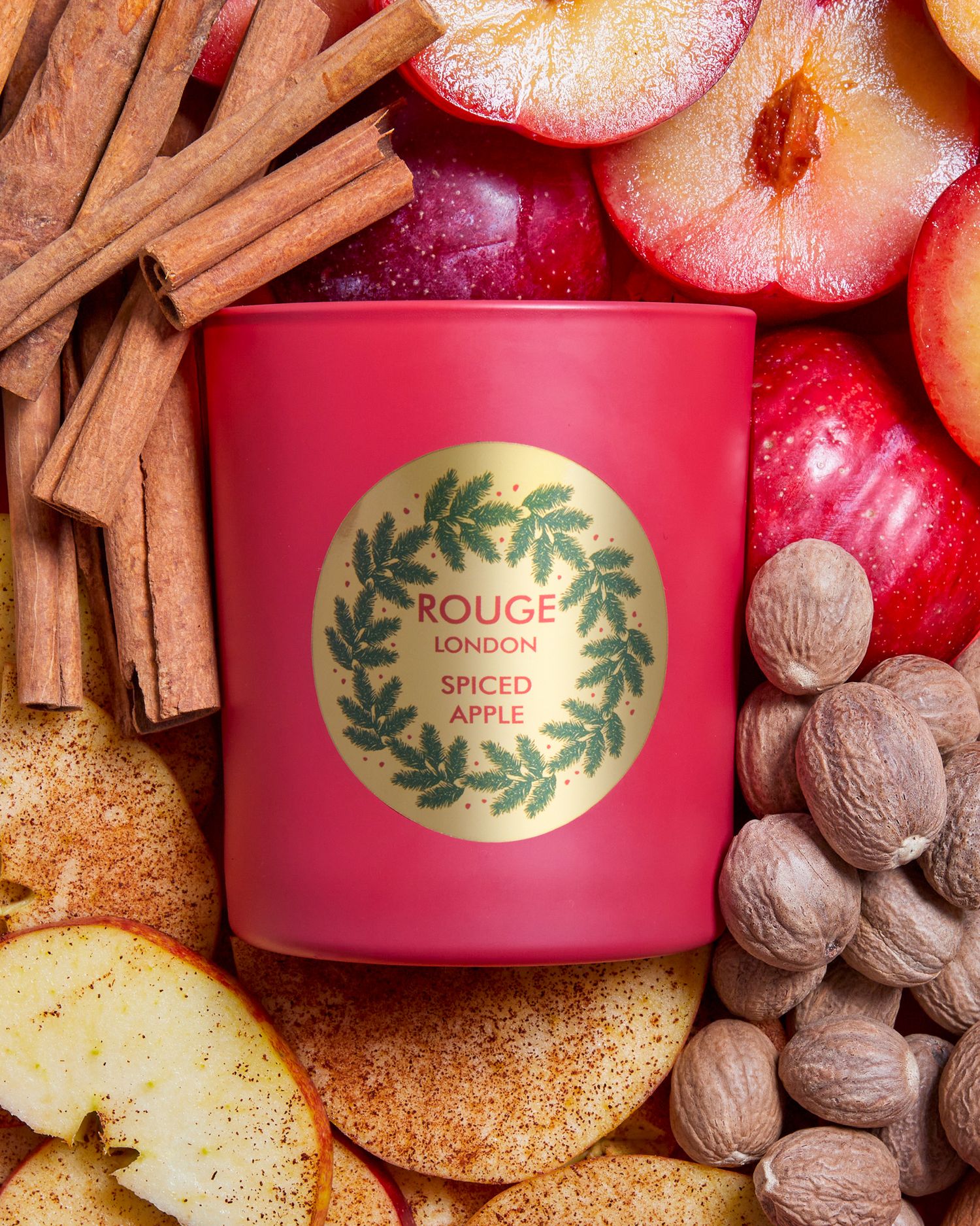 Red holiday candles surrounded by spices, apples, and nuts in a festive arrangement.