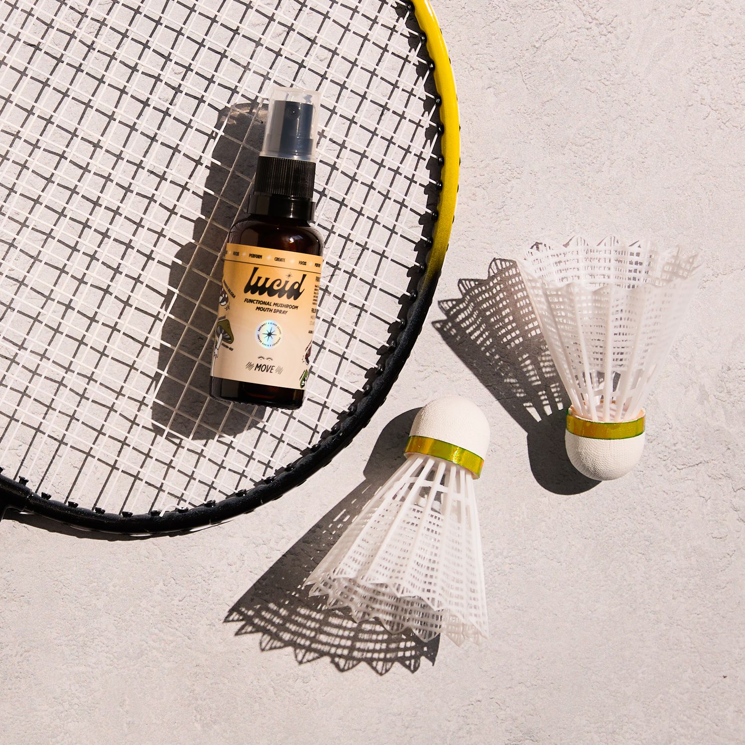 Small amber bottle next to badminton racket and shuttlecock creating geometric shadows.