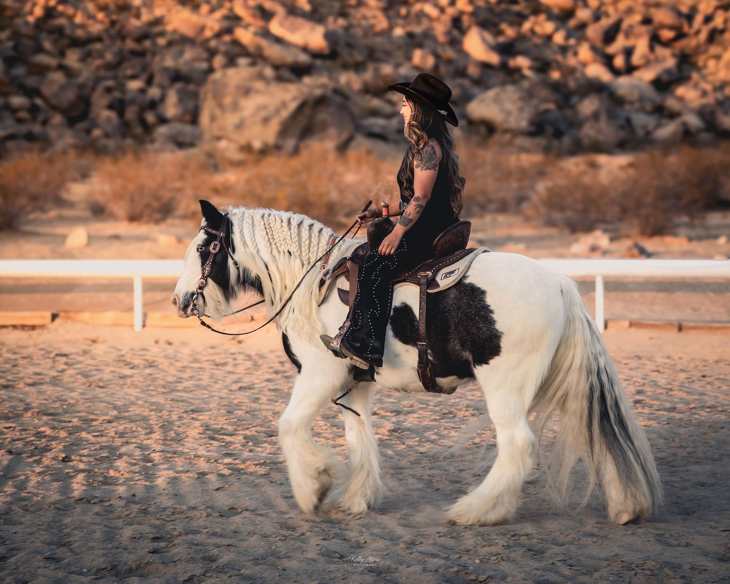 A white horse with long flowing mane walks through a desert arena at dusk.