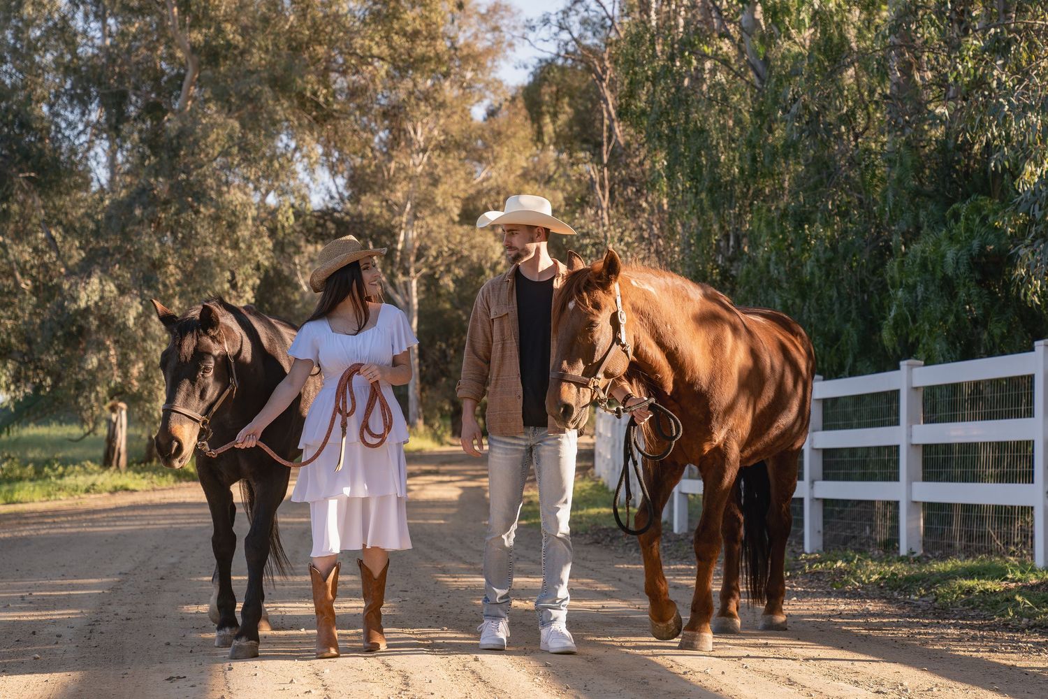 A brown horse and person walking along a white fence lined path during golden hour sunset.
