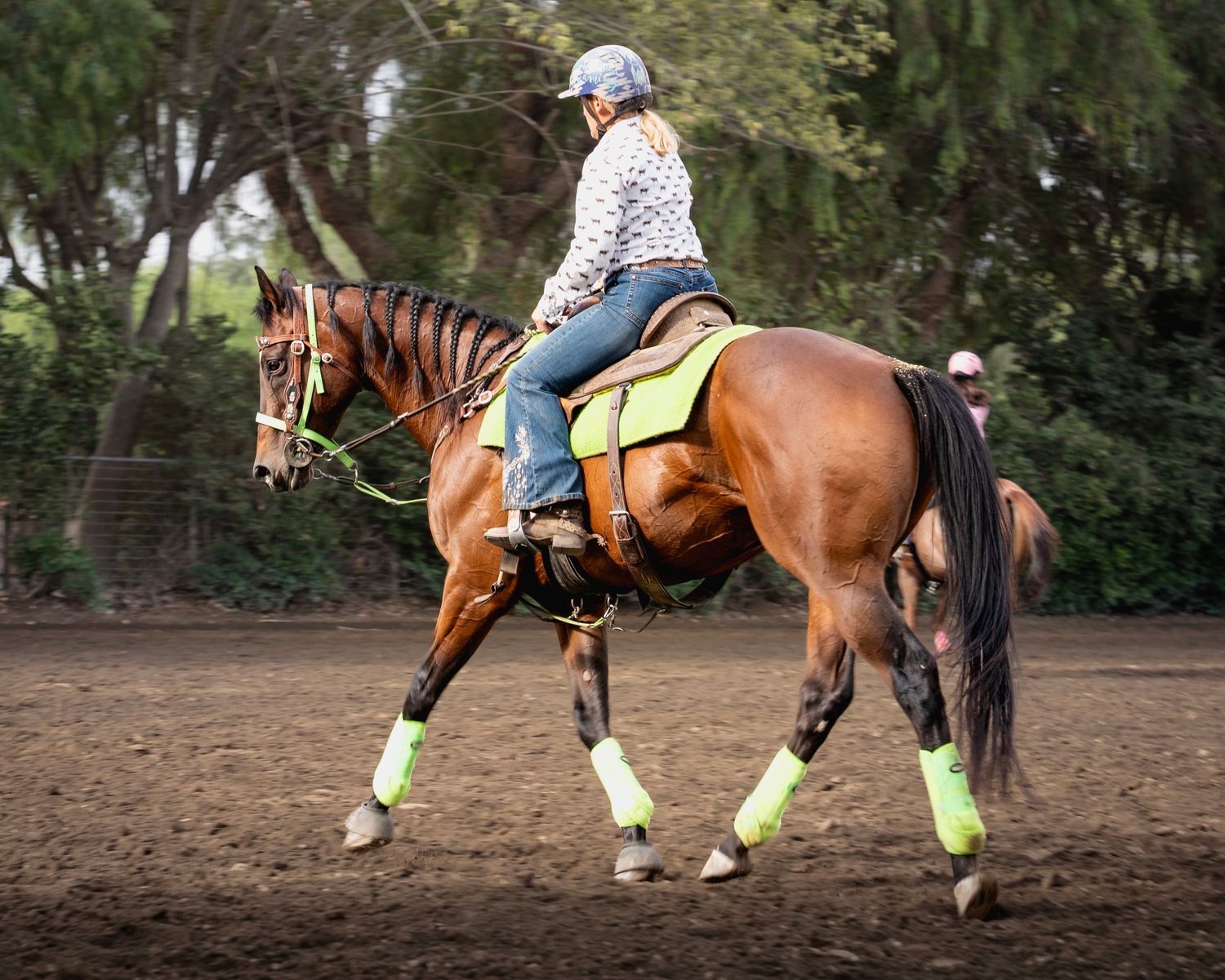 Horse and rider practicing barrel racing patterns with neon leg wraps in an outdoor arena.