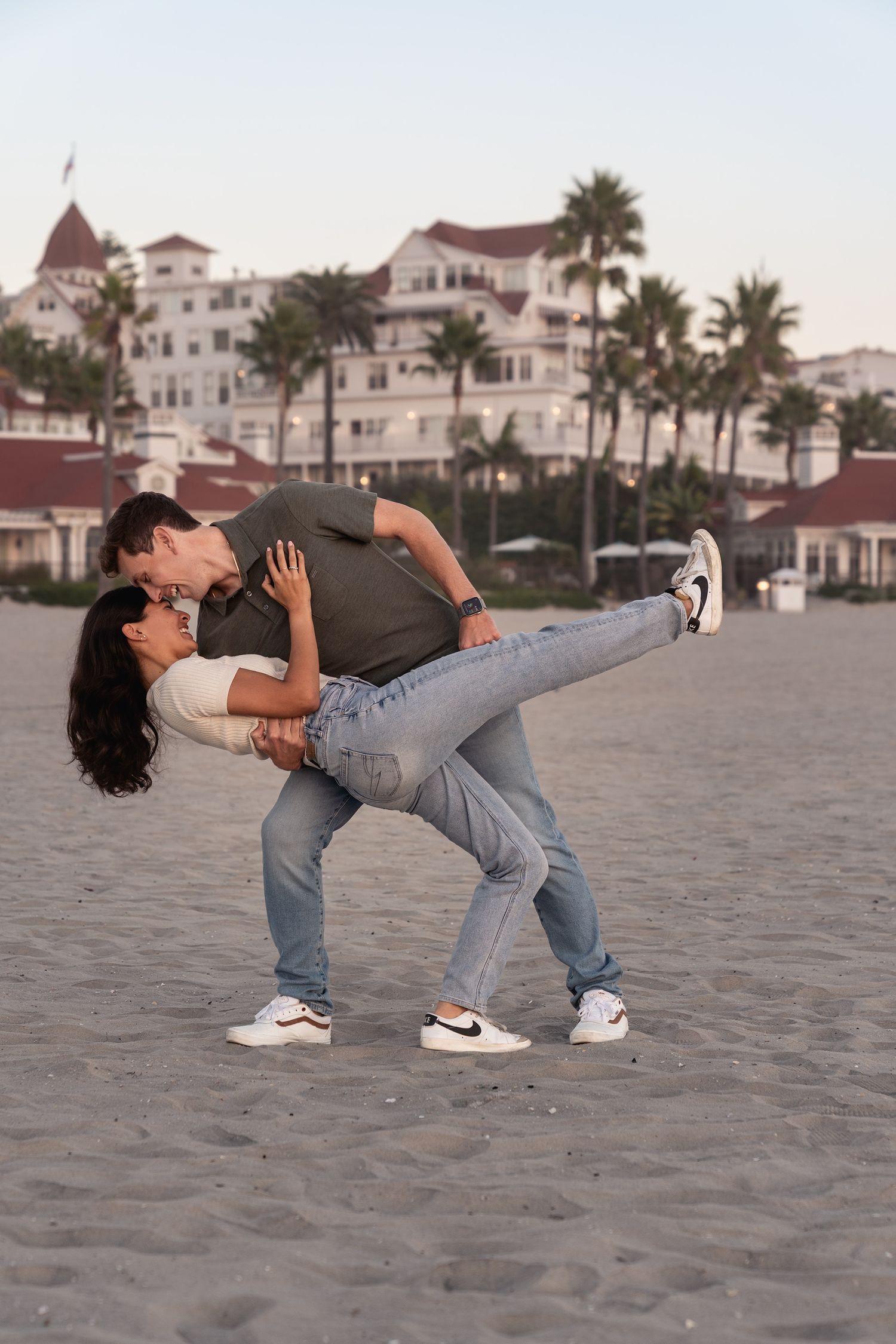 A playful dance dip sequence on the beach with coastal buildings in the background.