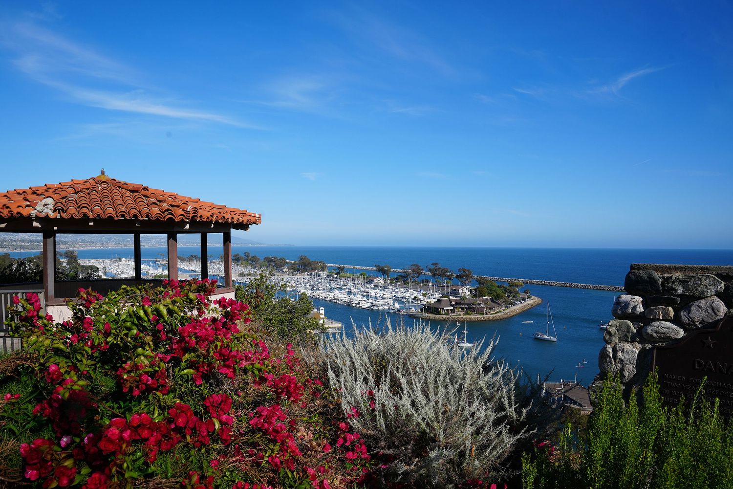 Scenic coastal views of Dana Point Harbor with red bougainvillea flowers and ocean vistas under blue skies.