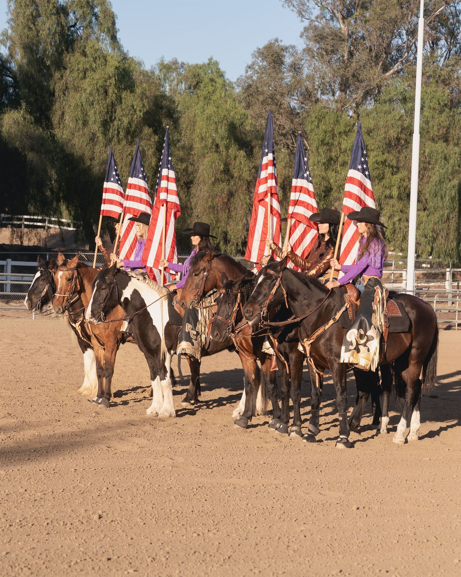 Line of horses and riders with American flags in formation at a western equestrian event.