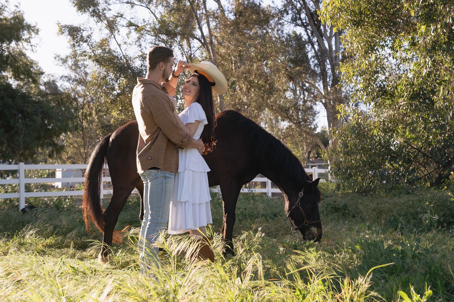 A couple embraces in a sunny outdoor setting with trees and natural scenery in the background.