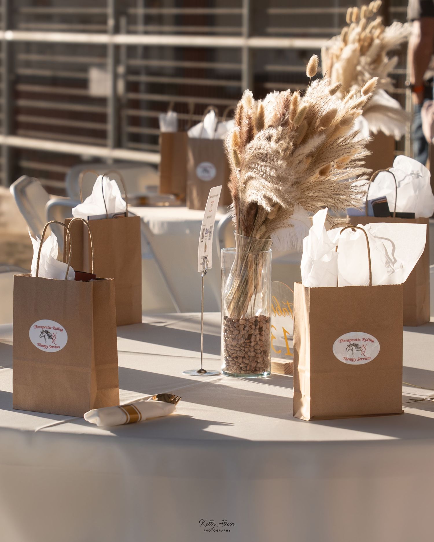 Brown paper gift bags with dried pampas grass arrangements displayed on a white table.