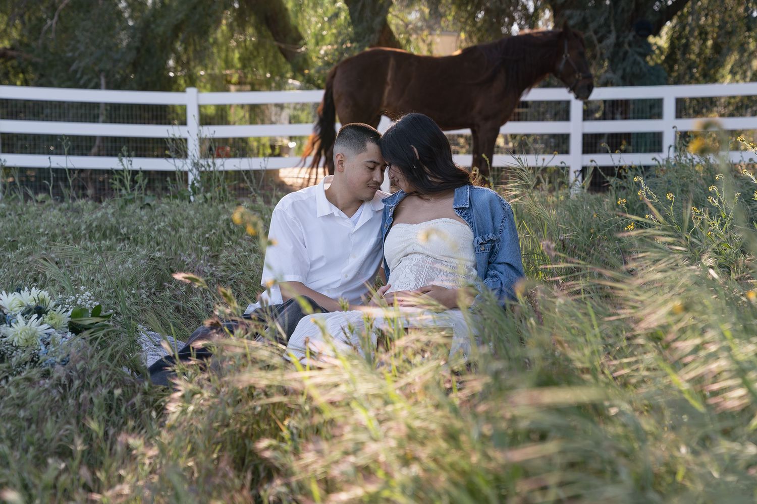 A couple sits together in a garden setting surrounded by tall grass and greenery on a sunny day.