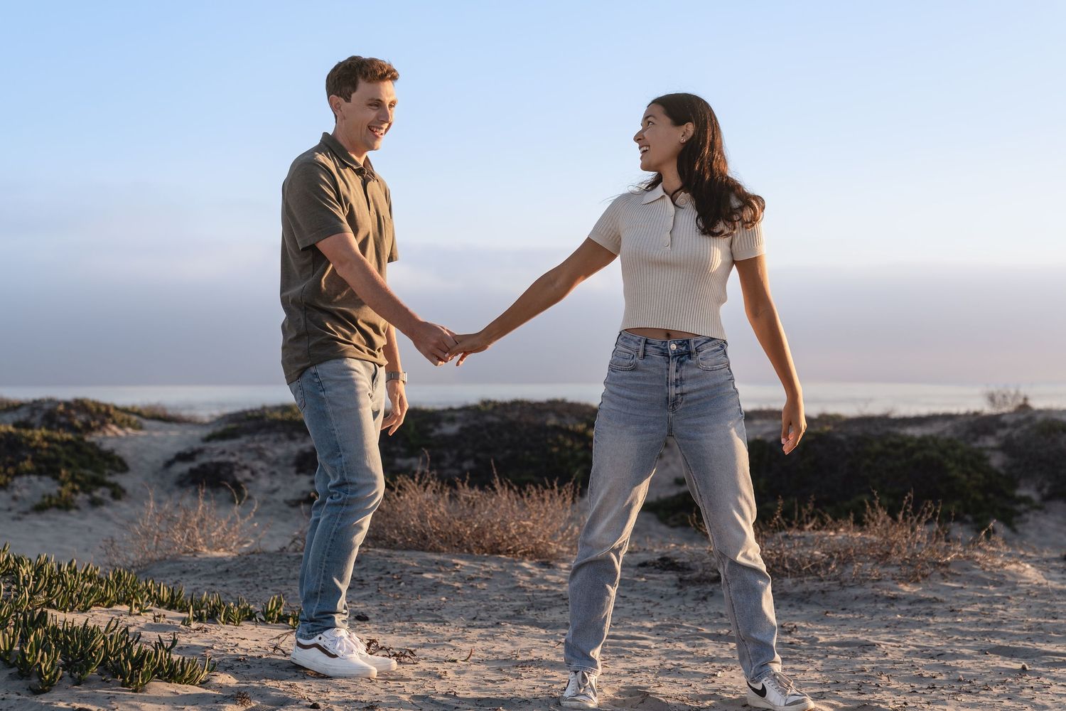 A couple dances playfully together on a sandy beach at dusk.