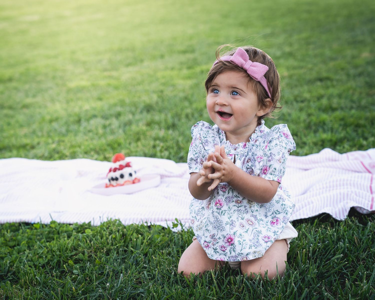 A joyful toddler laughing while sitting on a white blanket with a dessert.
