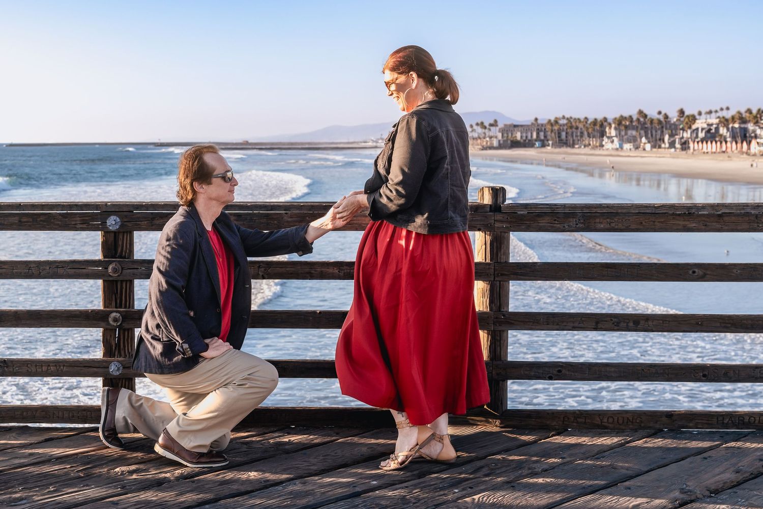 A couple shares a romantic moment on a beachfront pier during golden hour.