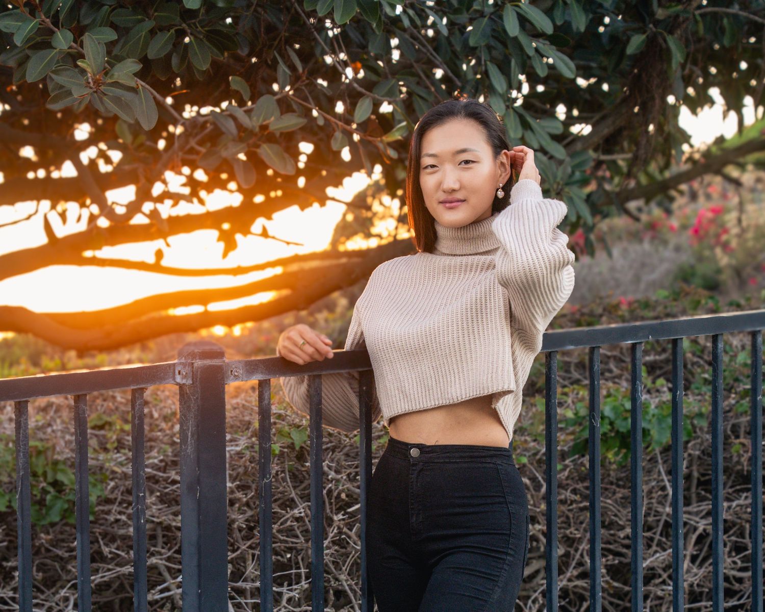 Person in cream sweater and dark pants standing near railing during golden hour.