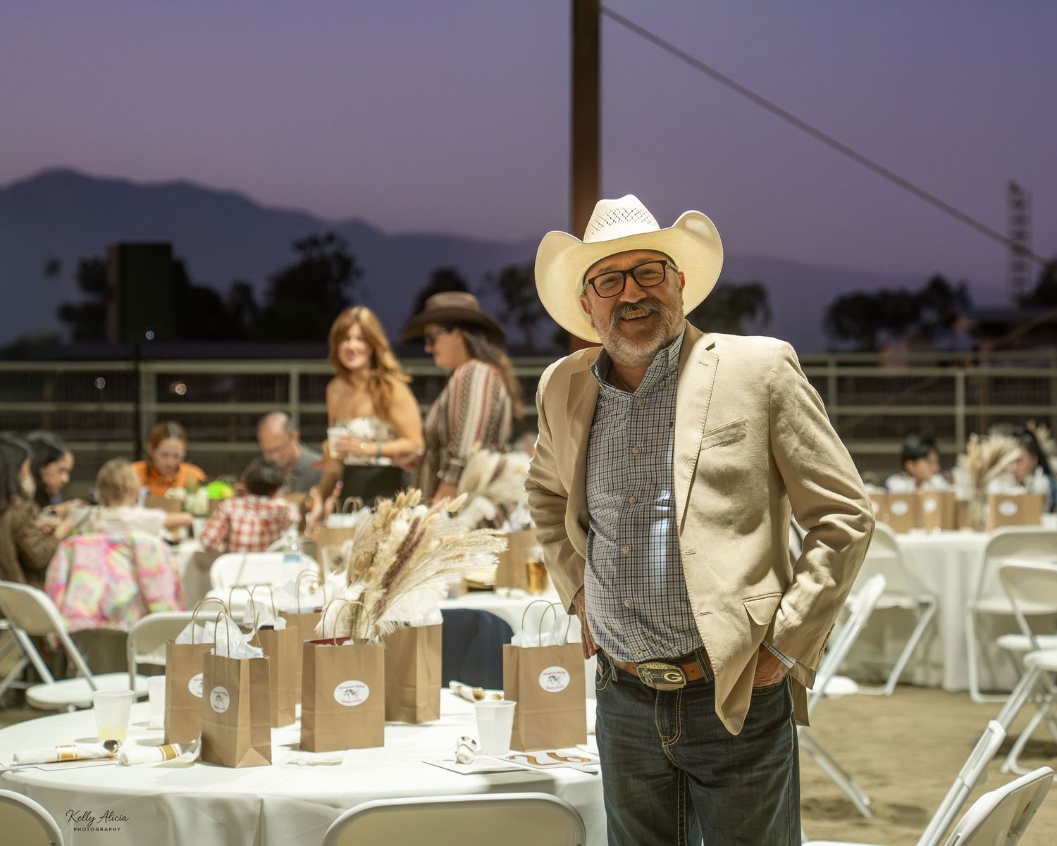 People gather at outdoor tables for a western-themed evening event with mountains visible in the background.