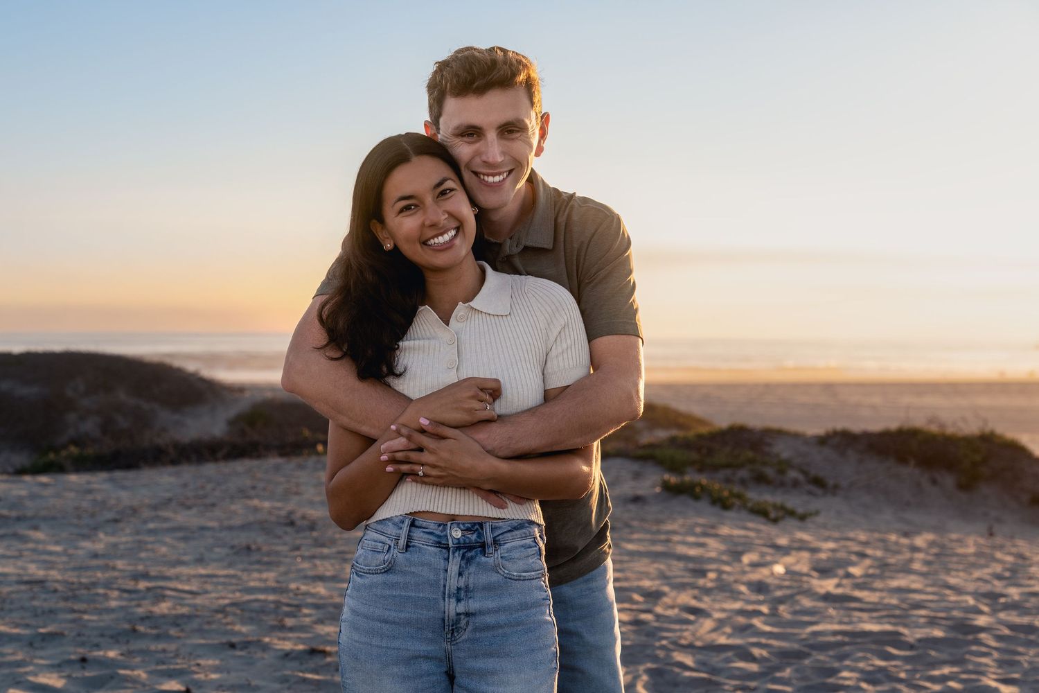 A couple shares joyful moments together on a beach during golden hour.