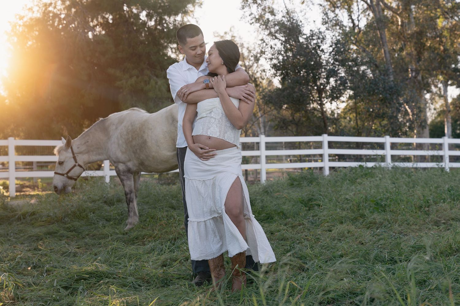 A couple shares a tender embrace in a grassy field during golden hour sunset.