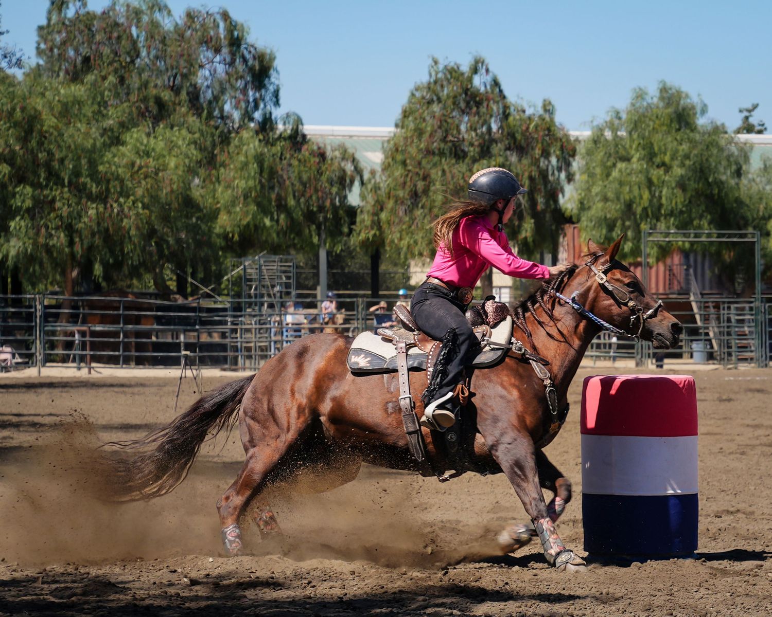 Barrel racing competitor on horseback rounding a turn in dusty arena.