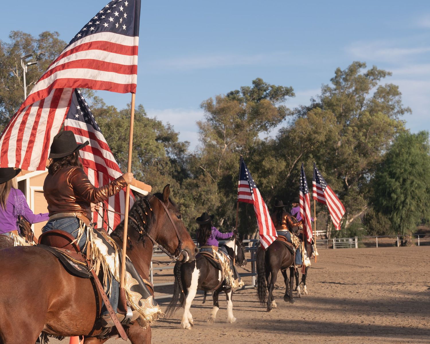Line of riders carrying American flags parade through western arena on horseback.