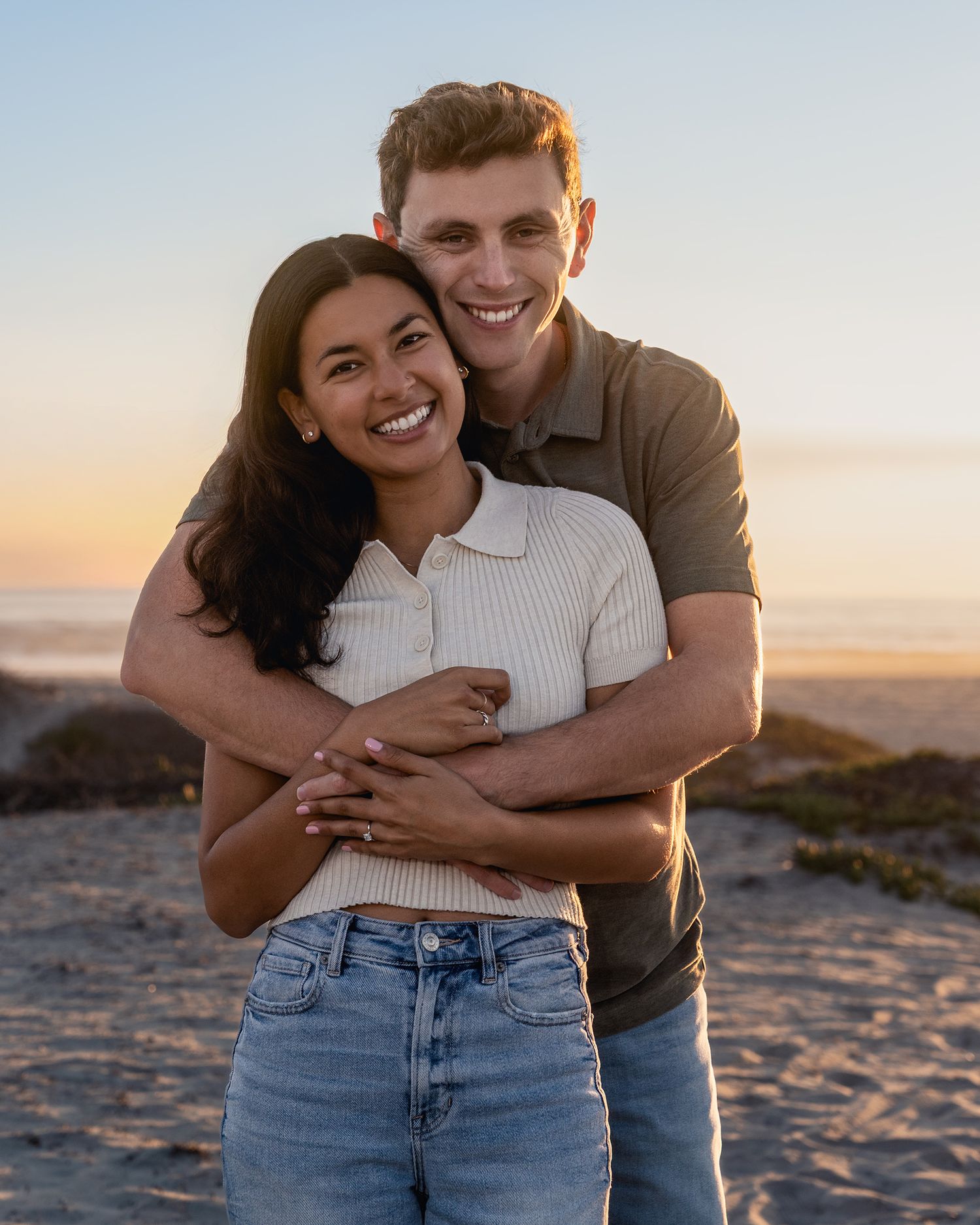 A couple embraces and laughs together on a beach during sunset.