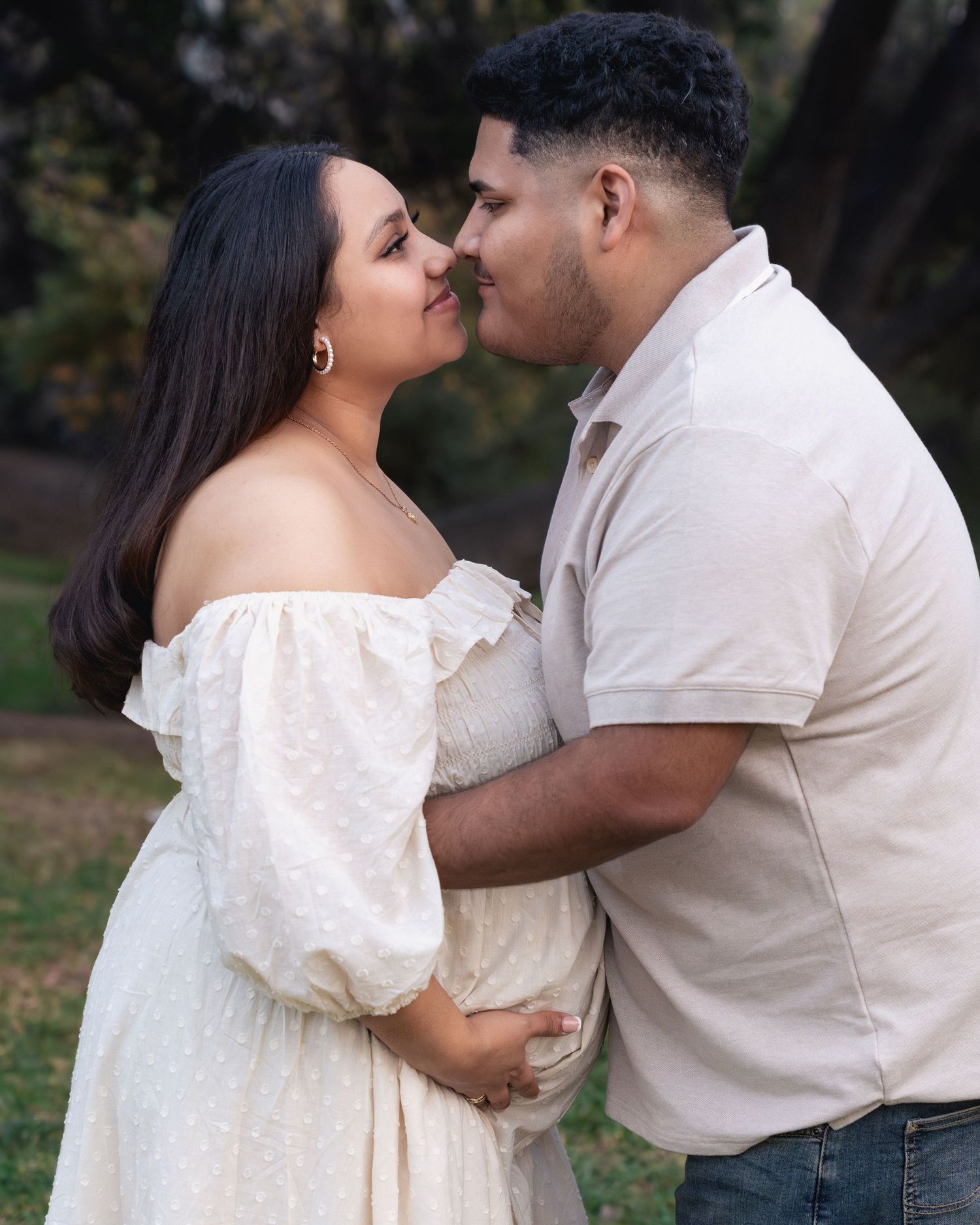 A romantic couple in white and beige outfits share tender moments during an outdoor photo session.