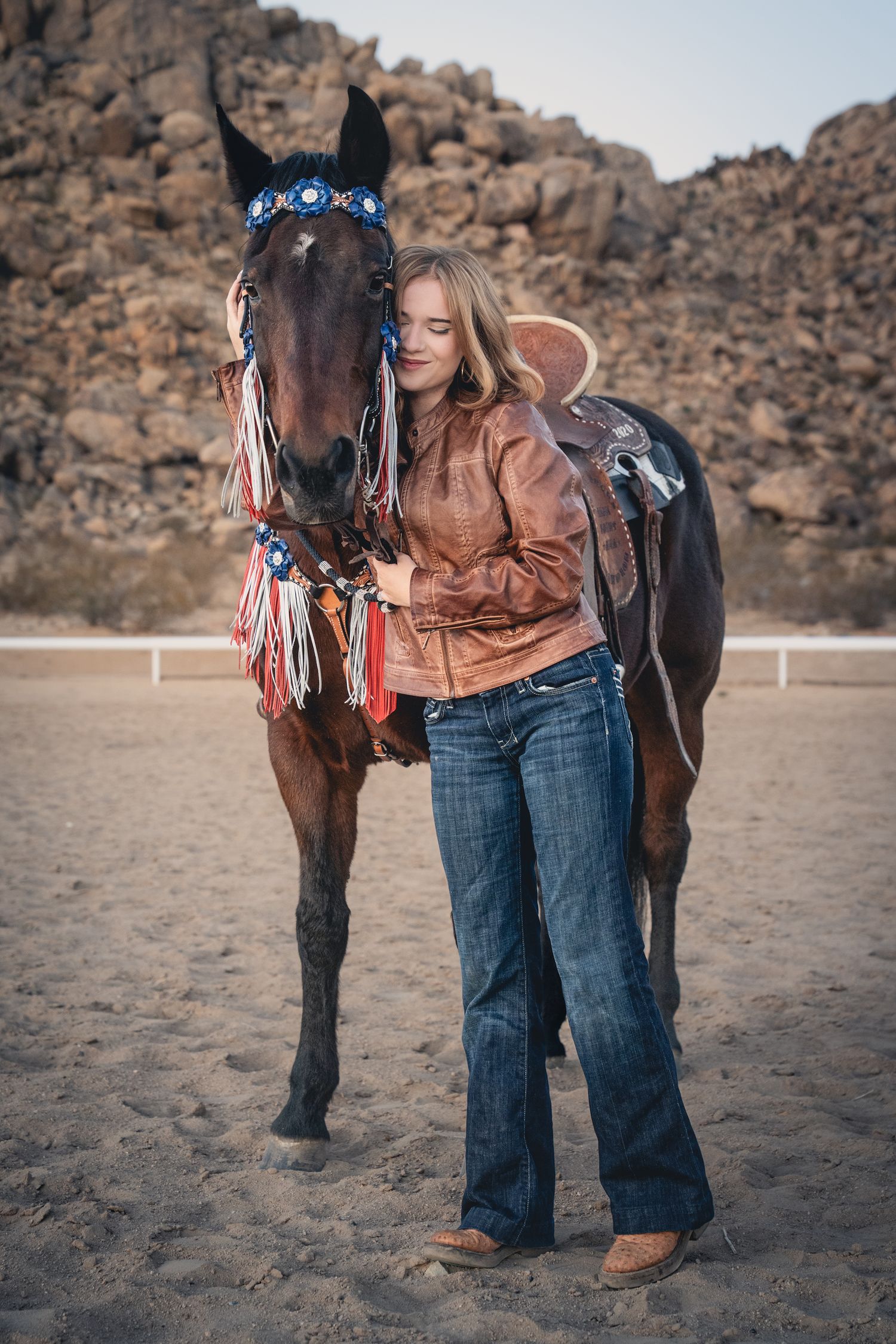 A horse wearing patriotic decorations stands in a desert arena.