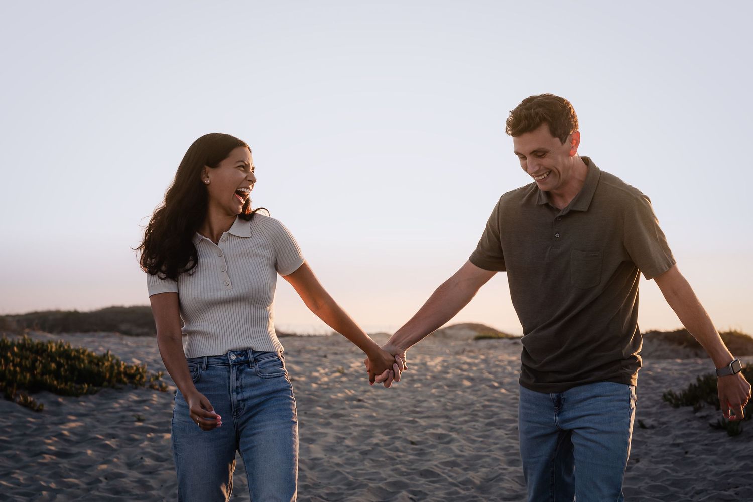 A romantic couple embraces on a sandy beach at sunset with the ocean in the background.