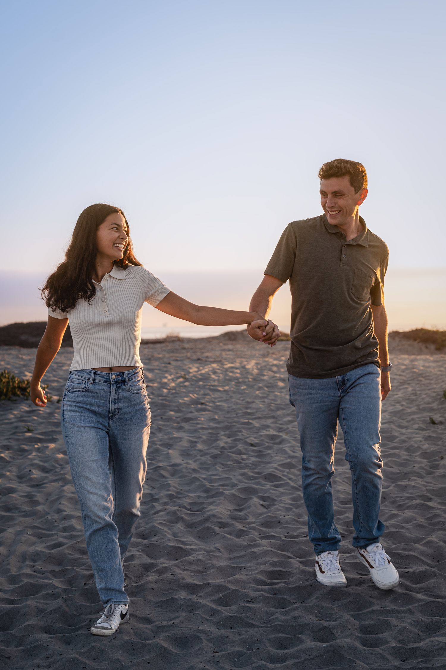 A couple holds hands while walking and dancing on the beach.