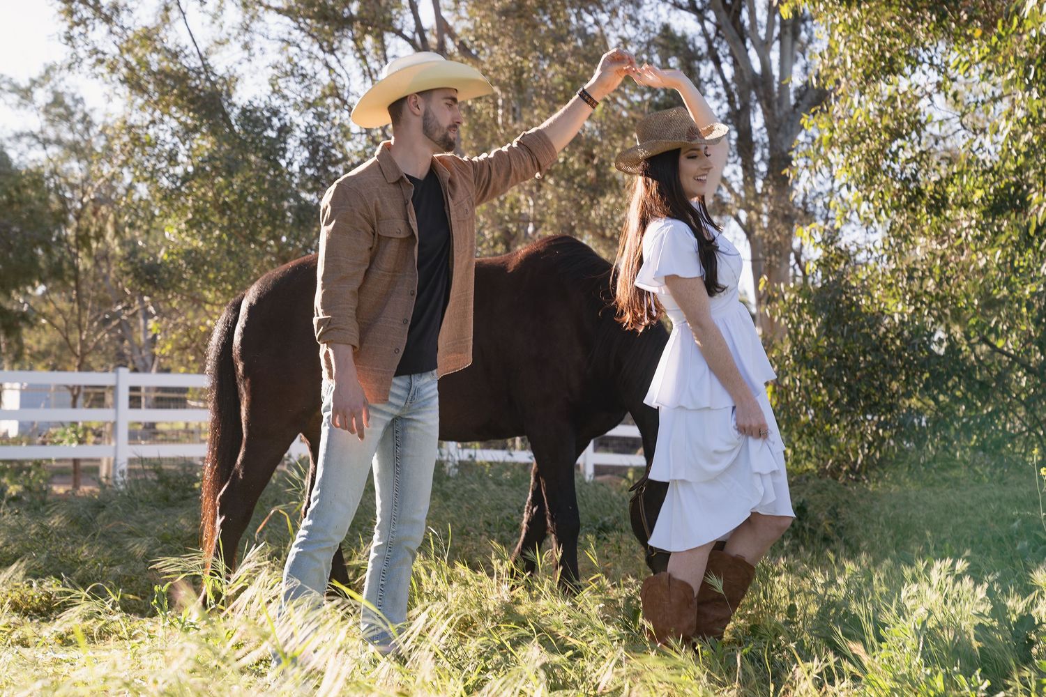 A couple in casual attire stands with their horse in a sunlit meadow during a photo session.