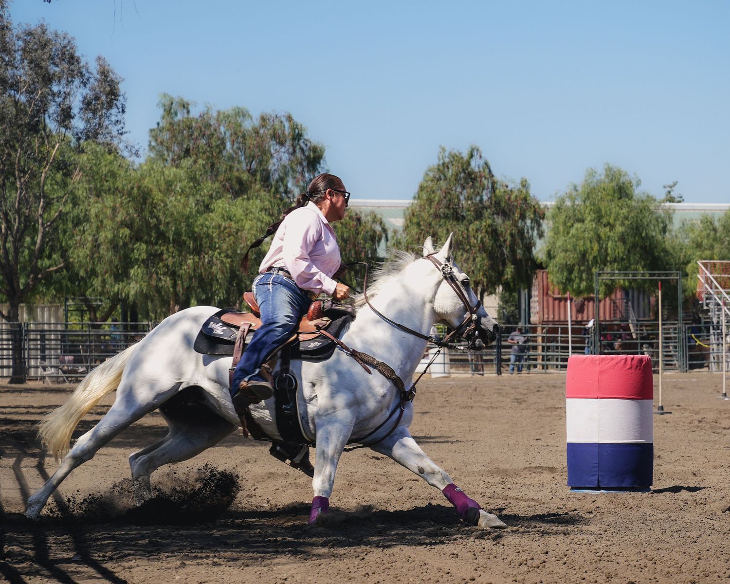 Horse and rider demonstrate barrel racing techniques in a sandy arena.