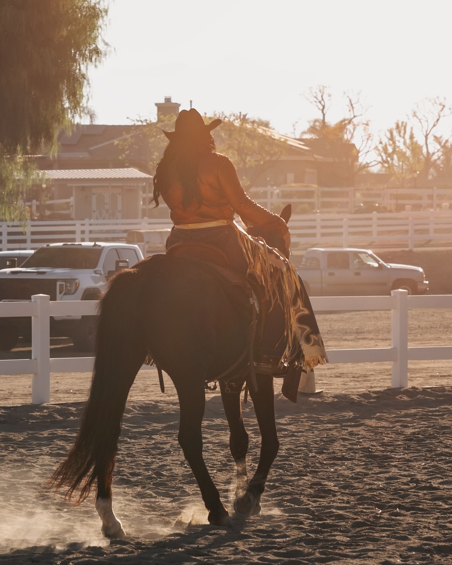 Silhouetted horse riders practicing in arena during golden sunset hour.