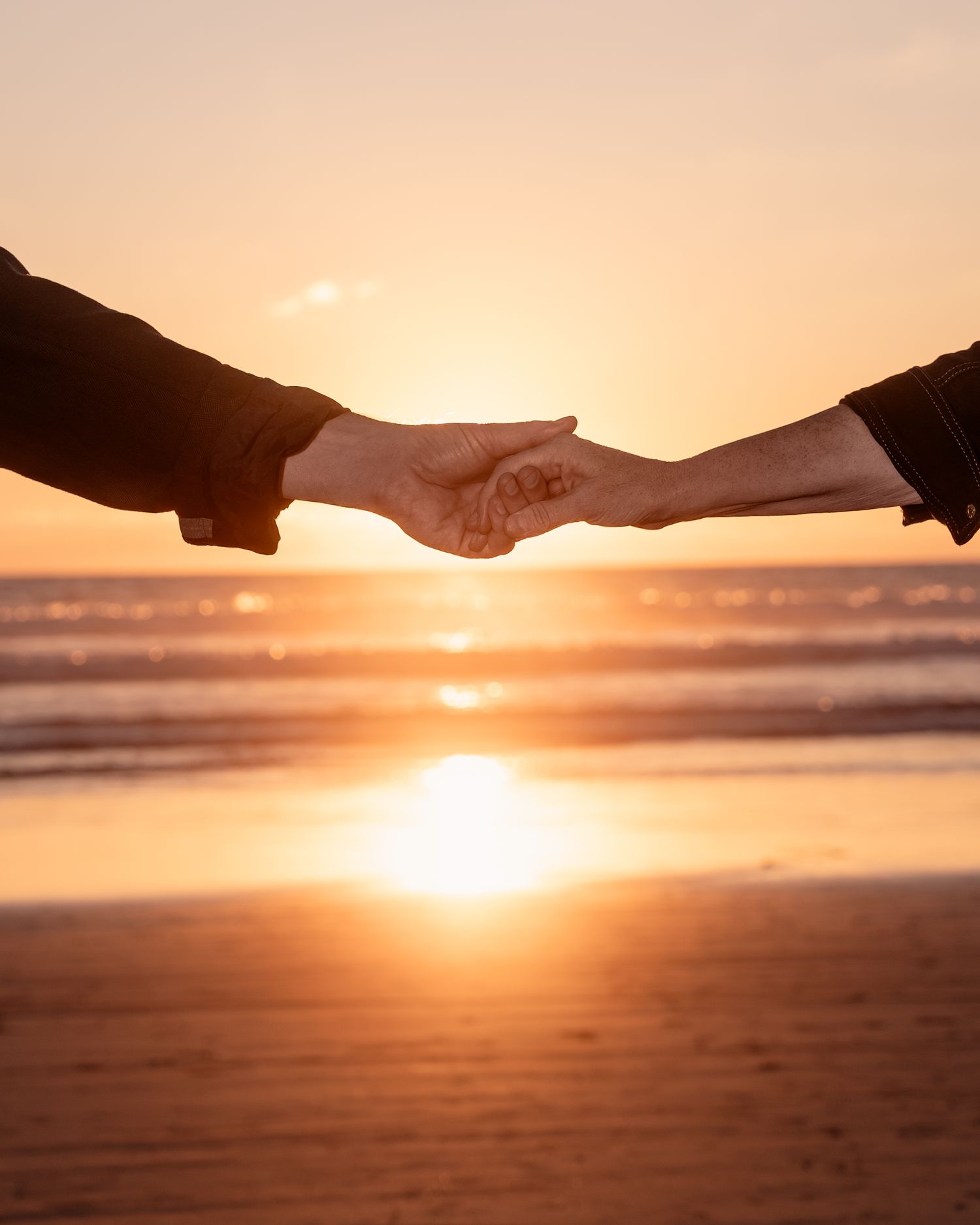 Hands reaching toward each other against sunset beach background.