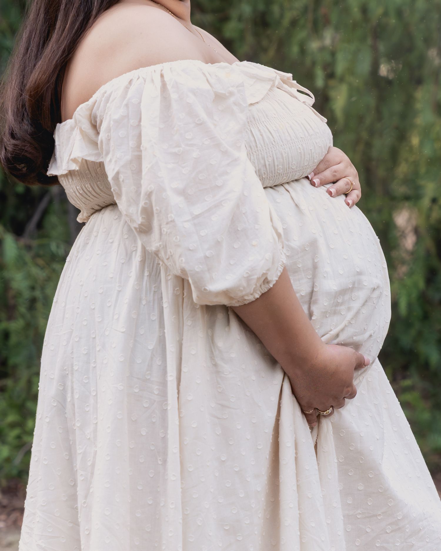 Person wearing white dress photographed from side against natural green background.