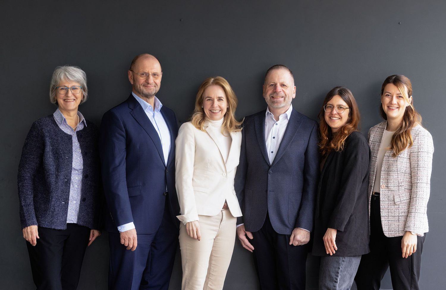 Business team in formal attire photographed against dark background in studio setting.