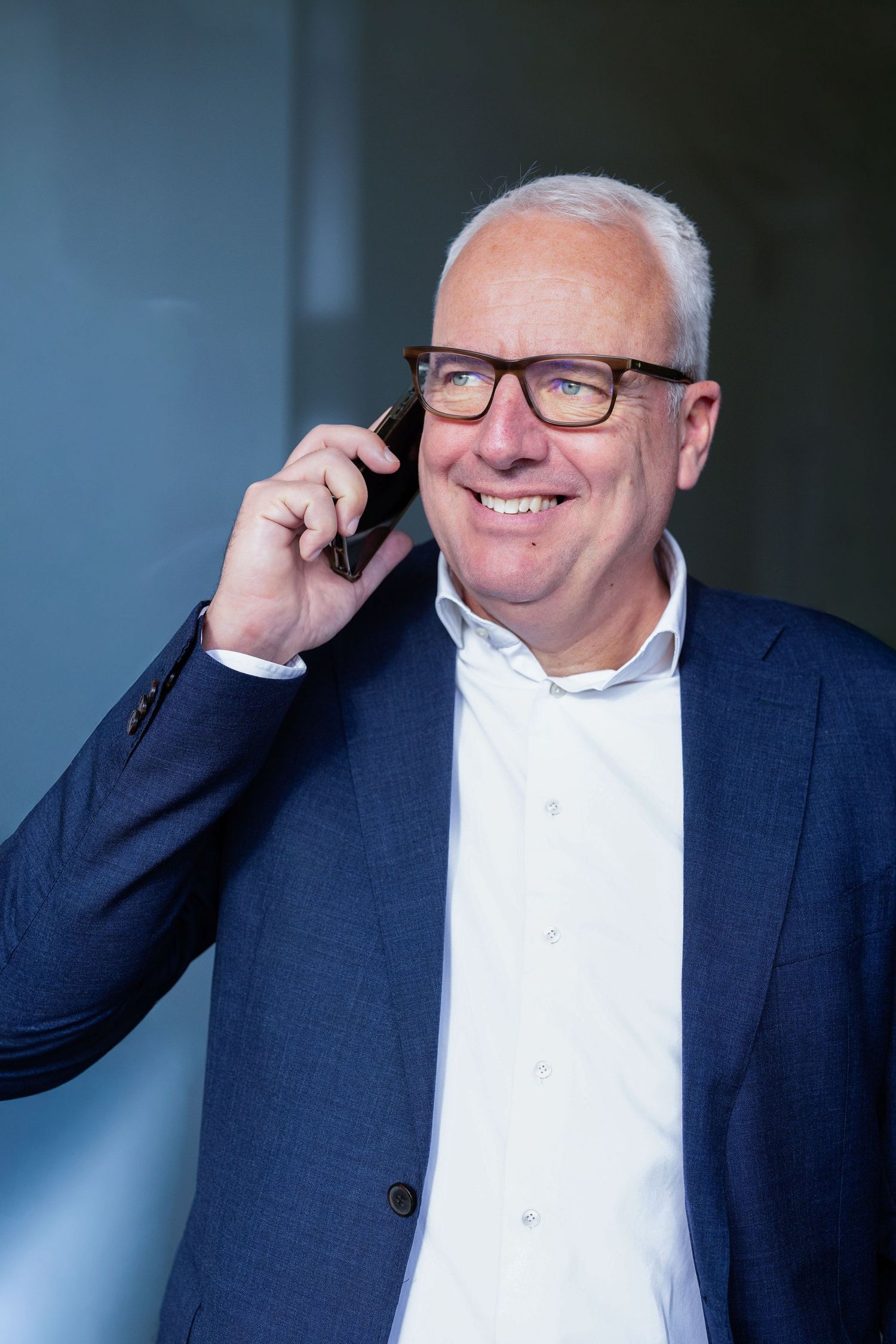 Business professional in navy blazer smiling while talking on phone in office.