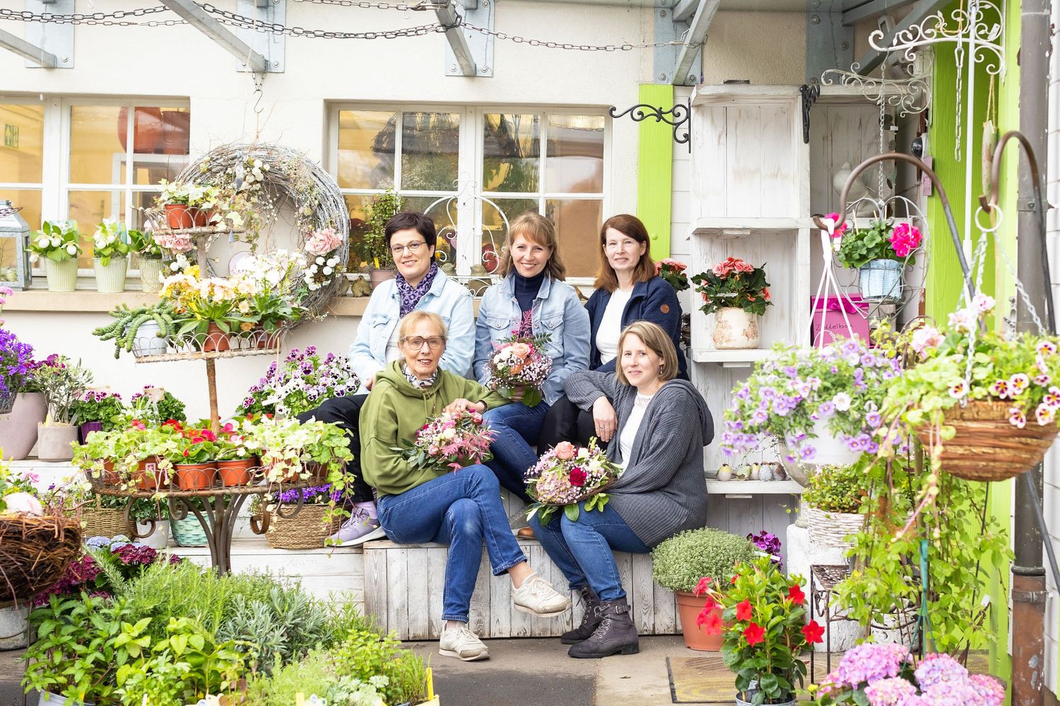 People gathered on garden steps surrounded by potted flowers and decorative outdoor decor.