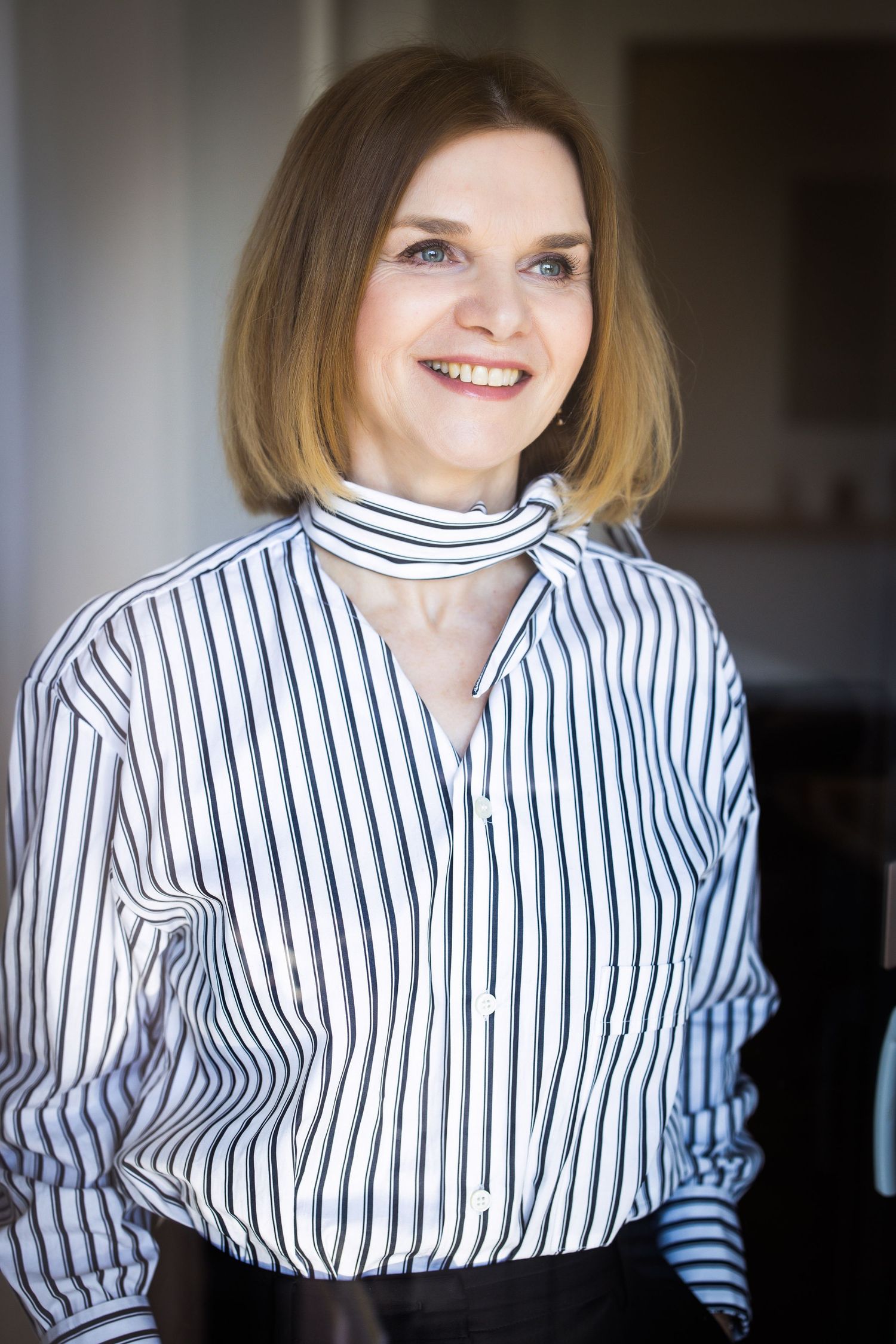 Professional portrait of person wearing striped button-down shirt with modern office background.