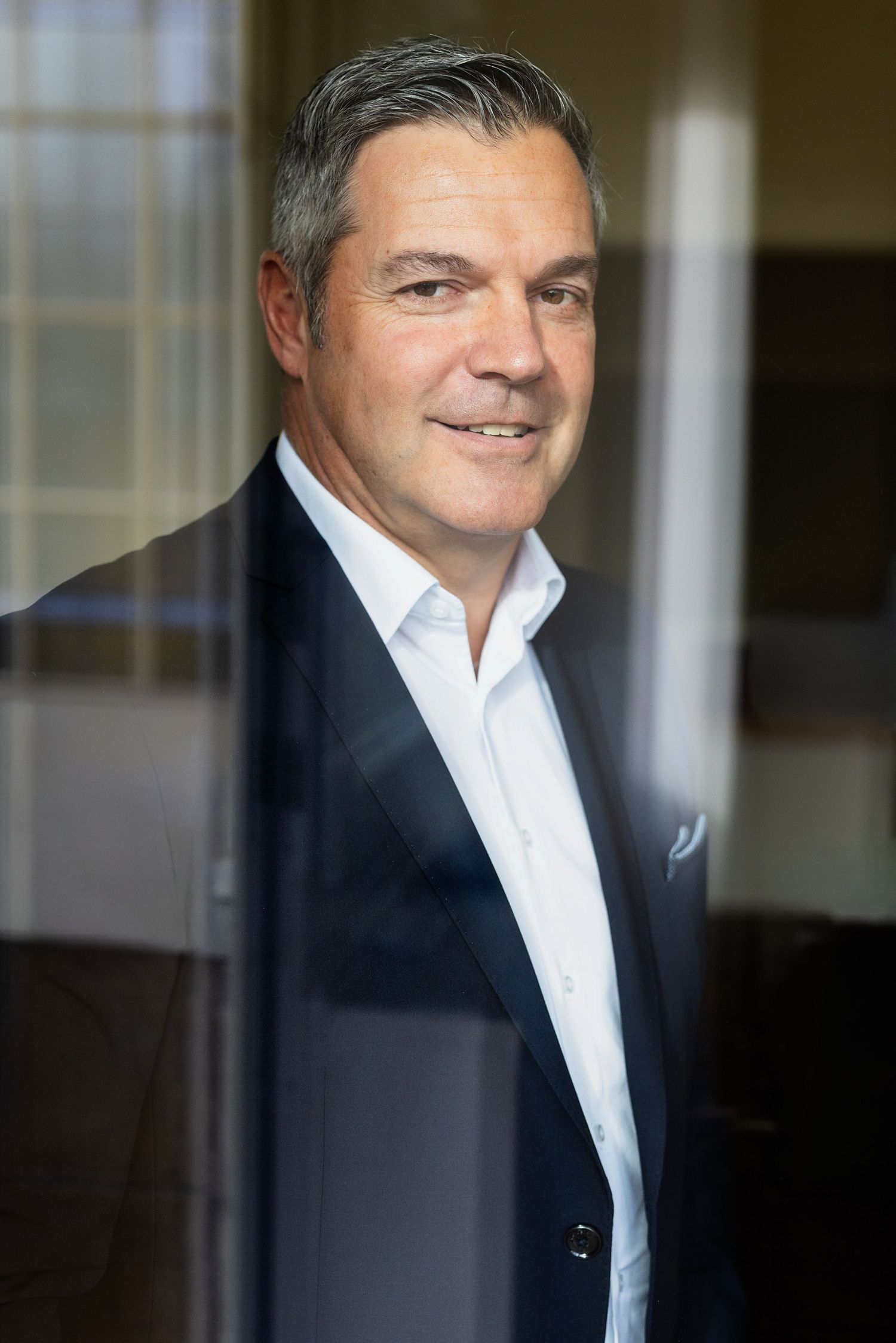 Corporate portrait of executive in dark suit and white shirt with natural lighting.