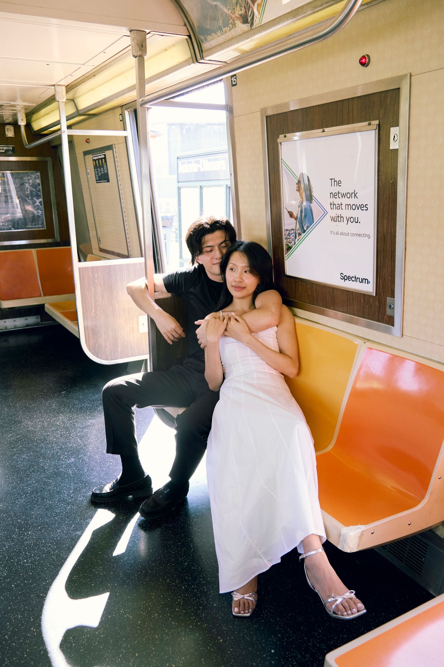 Couple sitting on orange subway seats inside a train car, sun streaming in through windows and casting long shadows.