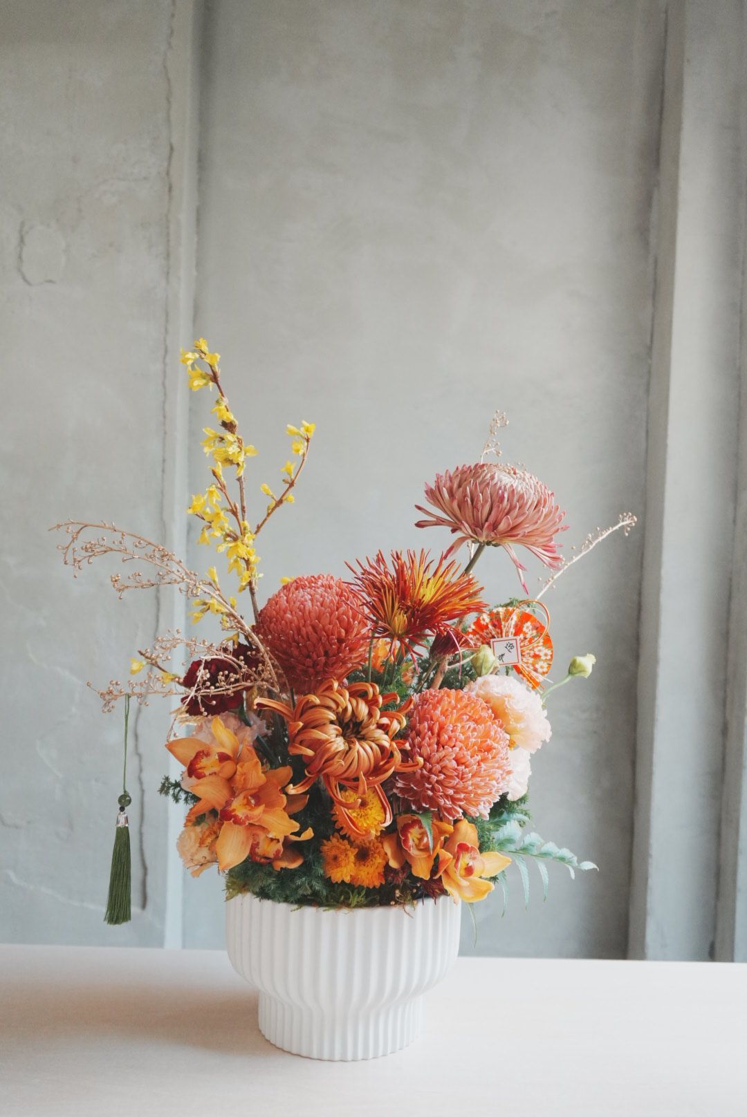 Modern floral arrangement featuring orange orchids, spider chrysanthemums, football mums, and seasonal blooms in a white ceramic vase.