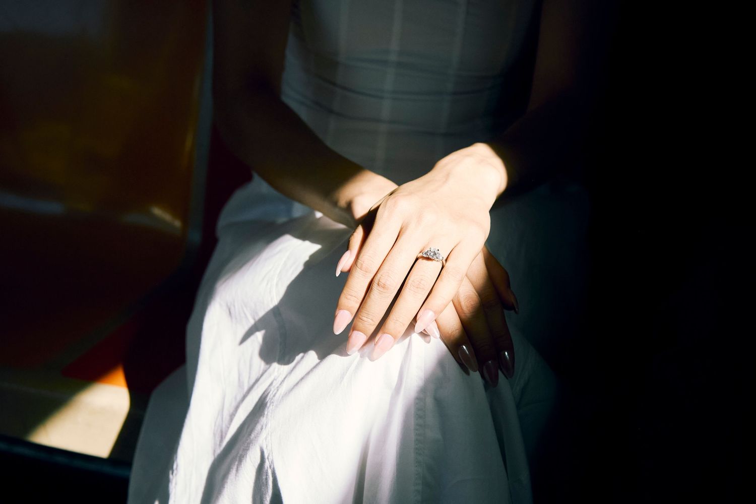 Close-up of a hand resting on fabric, with sharp window light and shadows across the scene.