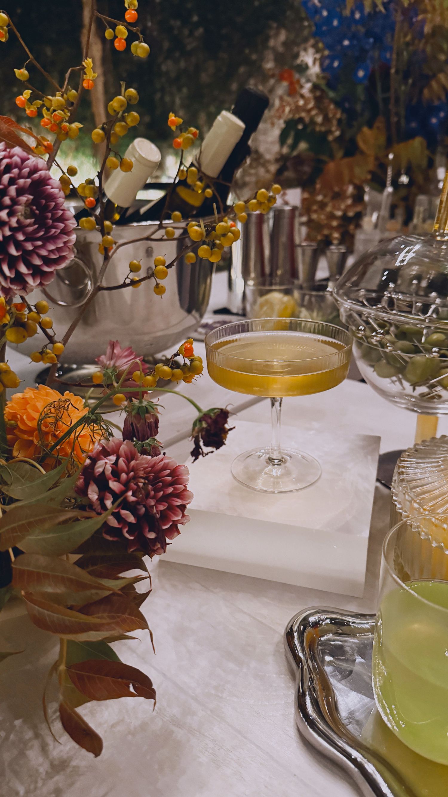 Styled table detail with a coupe cocktail, colorful florals, and glassware on a white tablecloth.