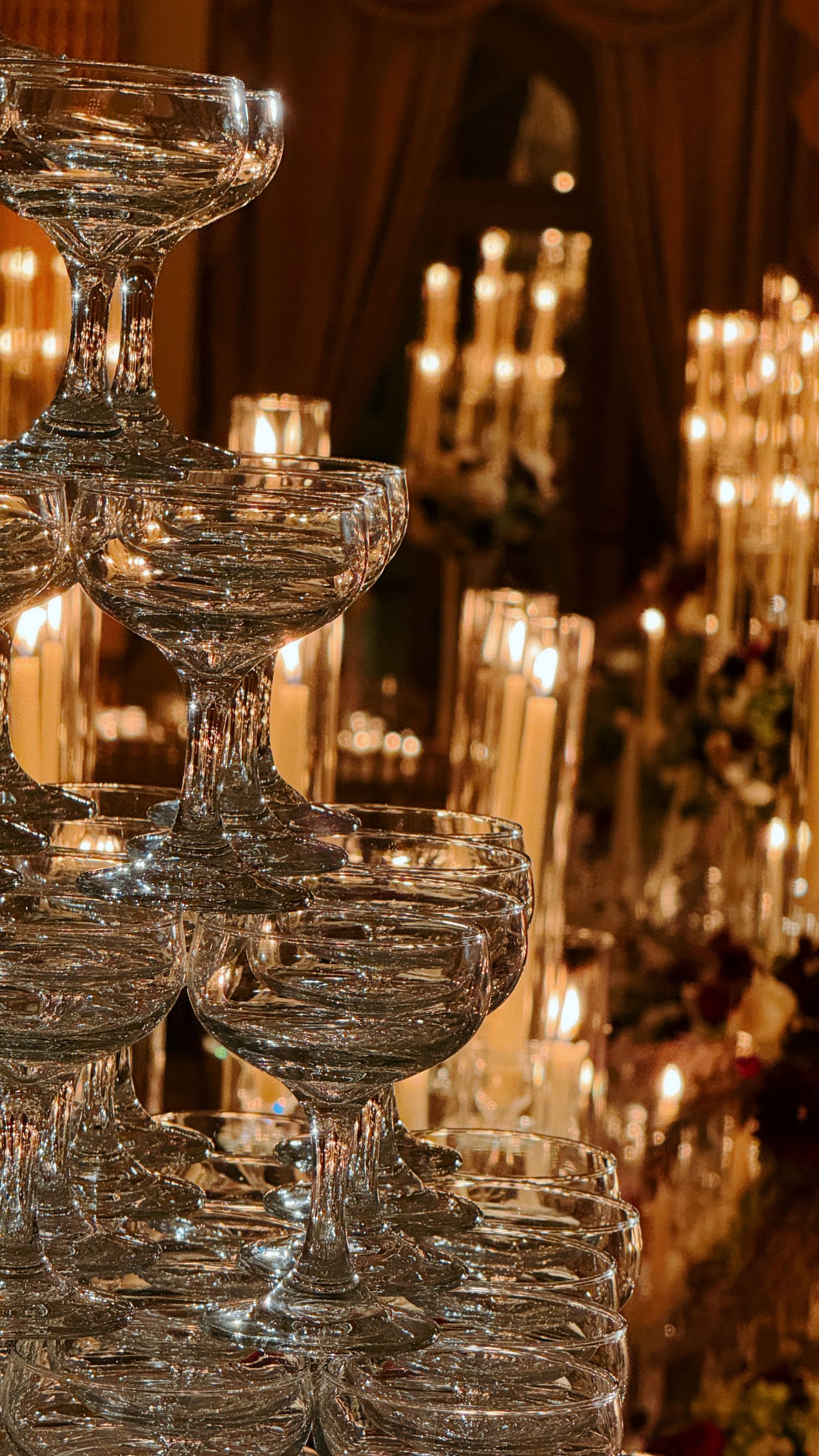 Stacked coupe glasses arranged like a tower, with warm candlelight glowing in the background.