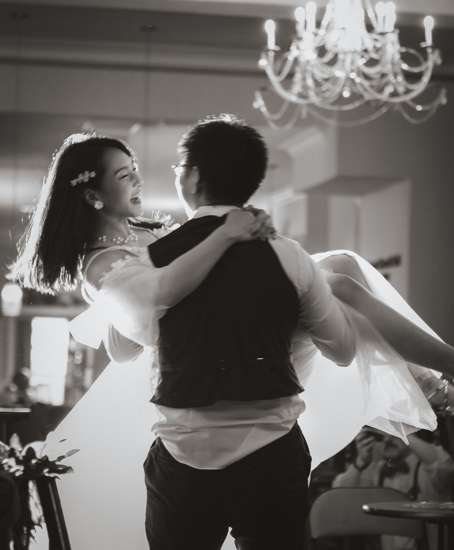 Groom carrying the bride during an intimate wedding reception, captured in a candid black-and-white editorial style.