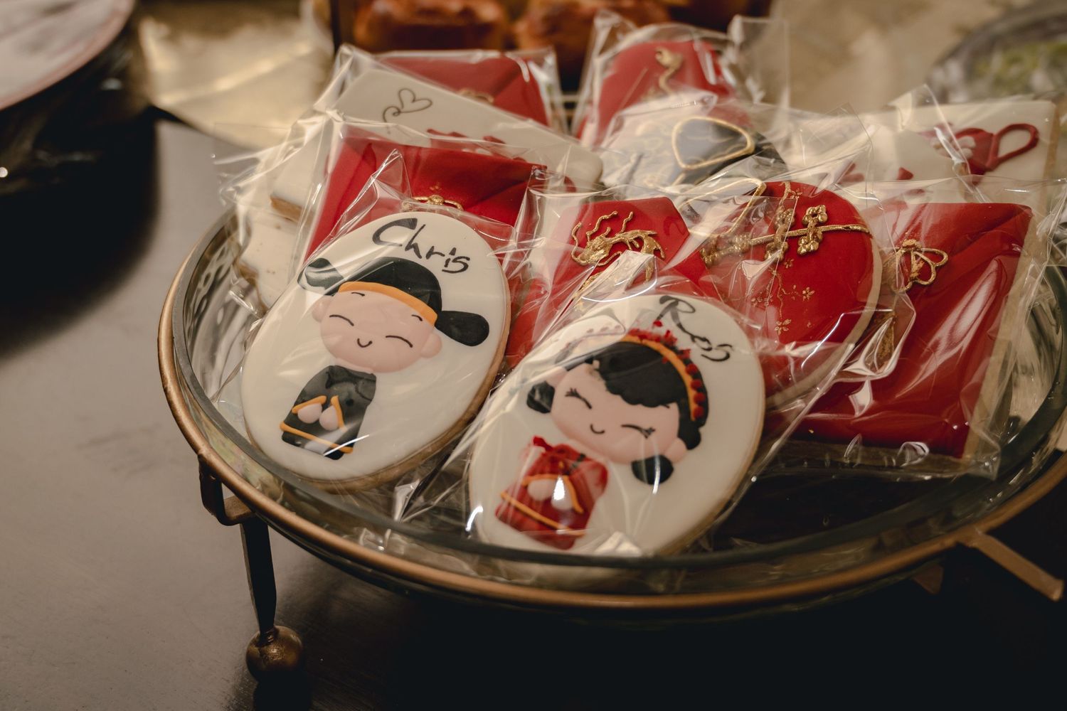 Close-up of decorated cookies wrapped in clear bags on a tray, featuring red and white designs and illustrated faces.