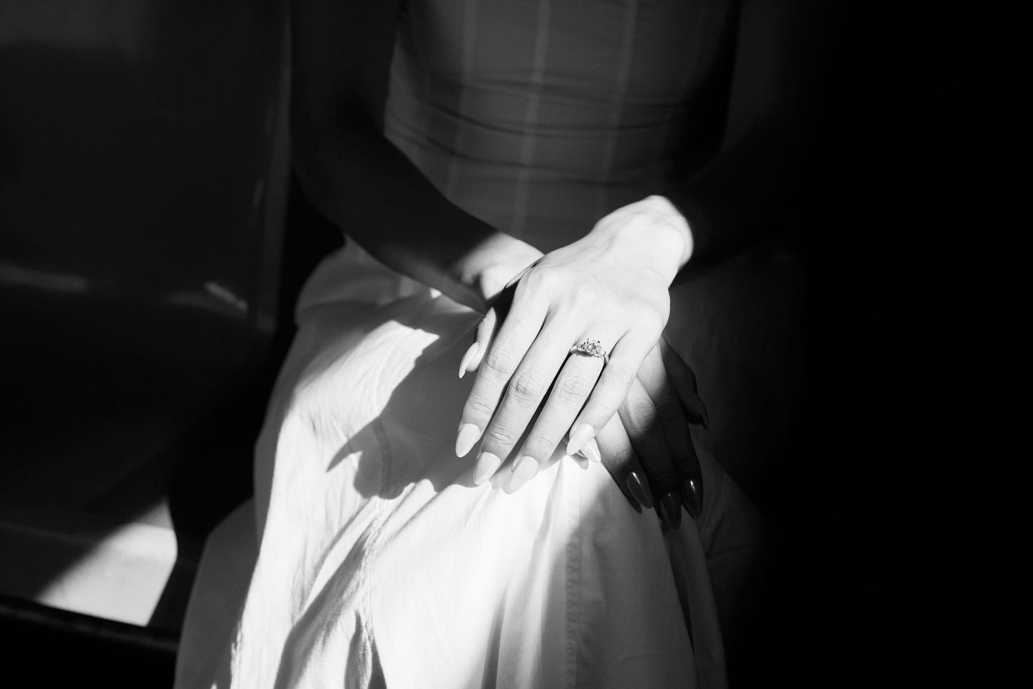 Black-and-white close-up of a hand resting on fabric, with sharp window light and shadows across the scene.